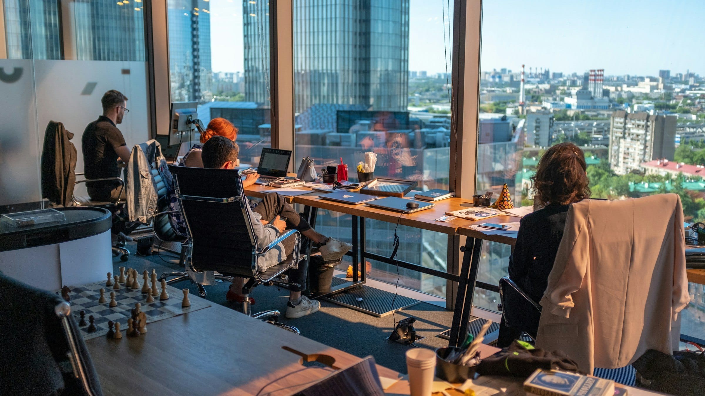 Oficina con ventanales y vista a la ciudad, con personas trabajando por la tarde